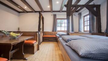 Een kamer met houten balken, een houten tafel met een schaal fruit, een bank en een bed met kussens.
