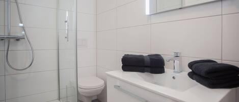 A modern bathroom with a glass shower enclosure, a white toilet, and a white sink with two towels.