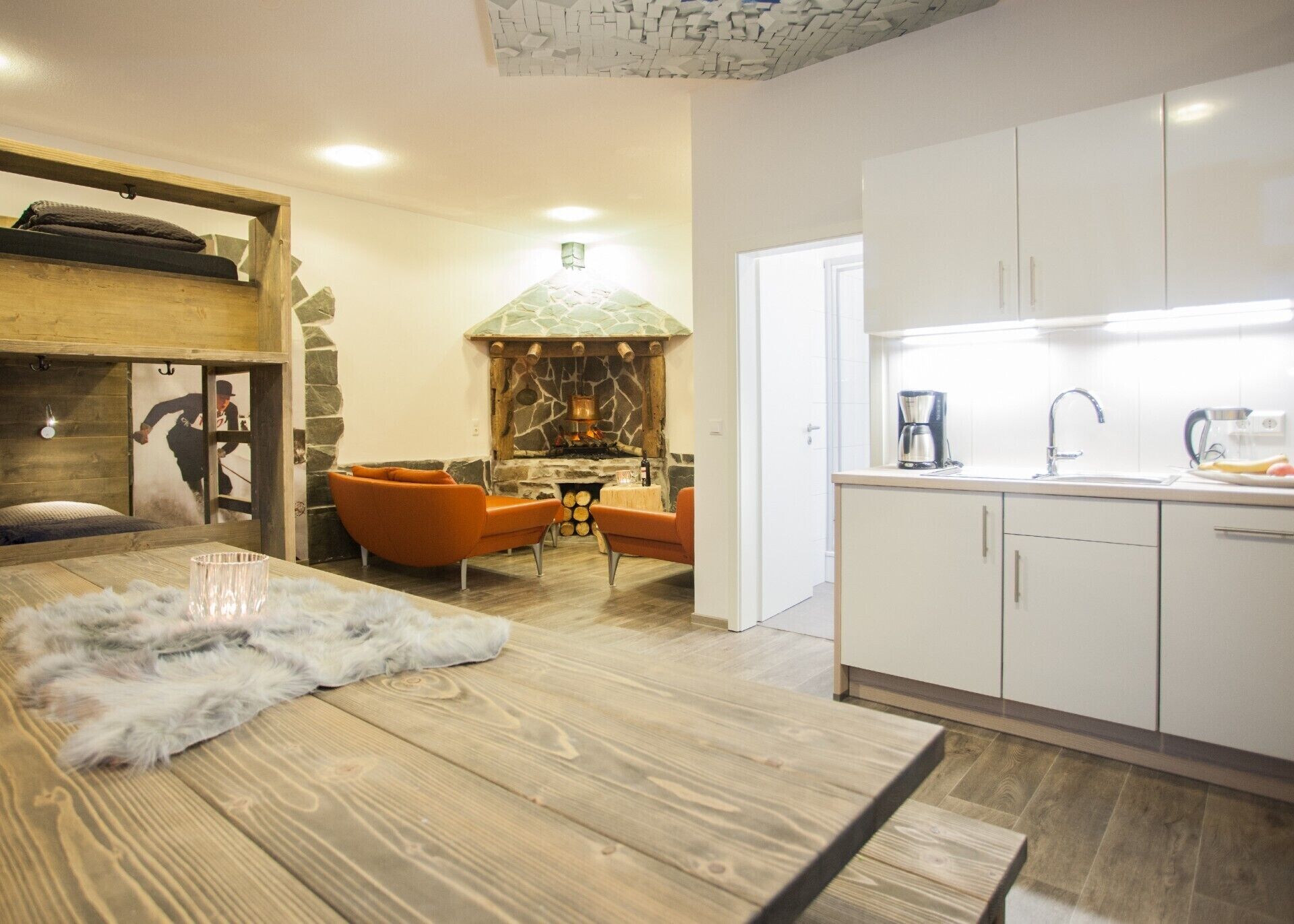 A cozy living area with a stone fireplace, wooden furniture, and a modern kitchen with white cabinets.