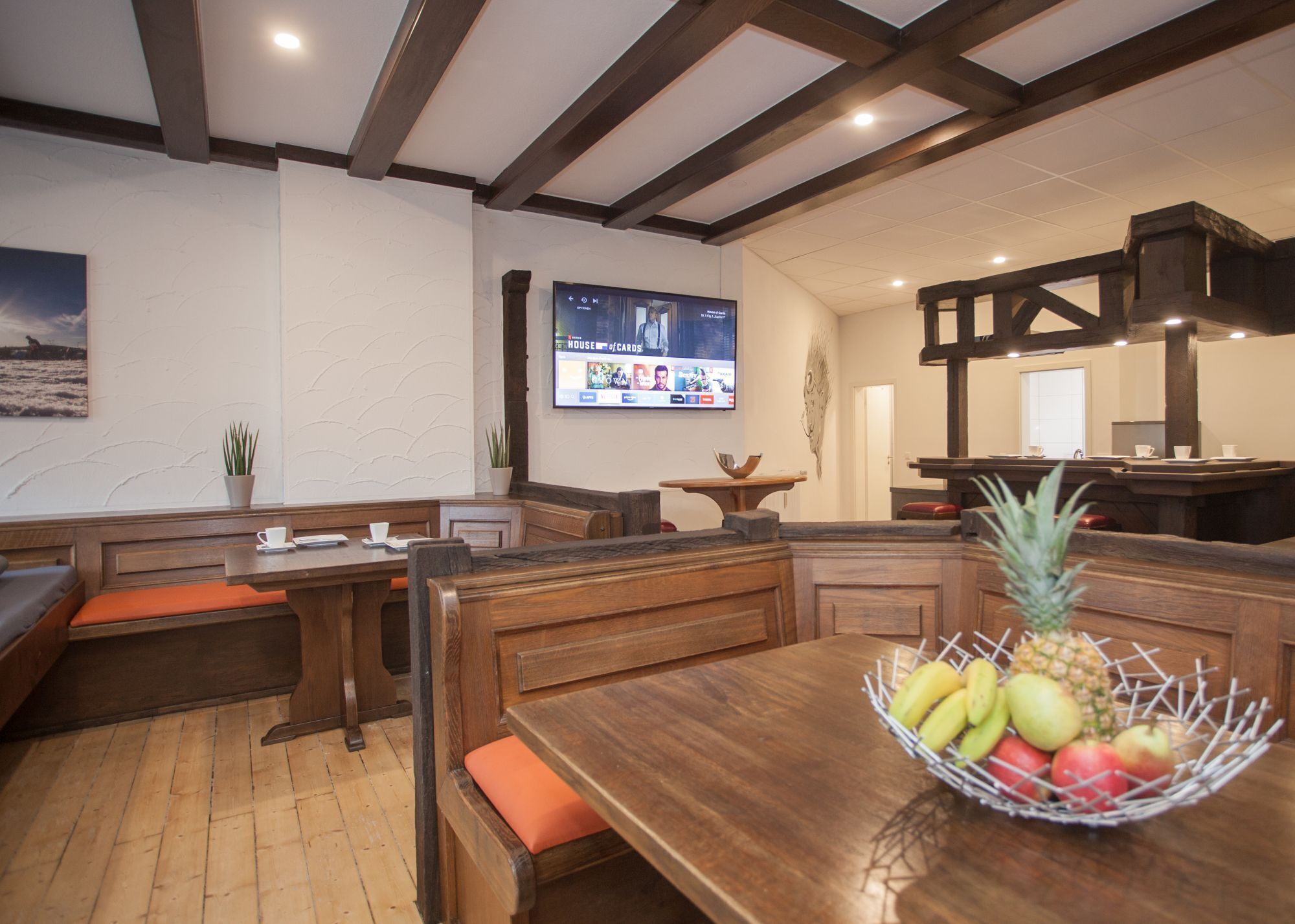 Un restaurante con cabinas de madera, una pantalla de televisión mostrando un programa y una cesta de frutas sobre la mesa.