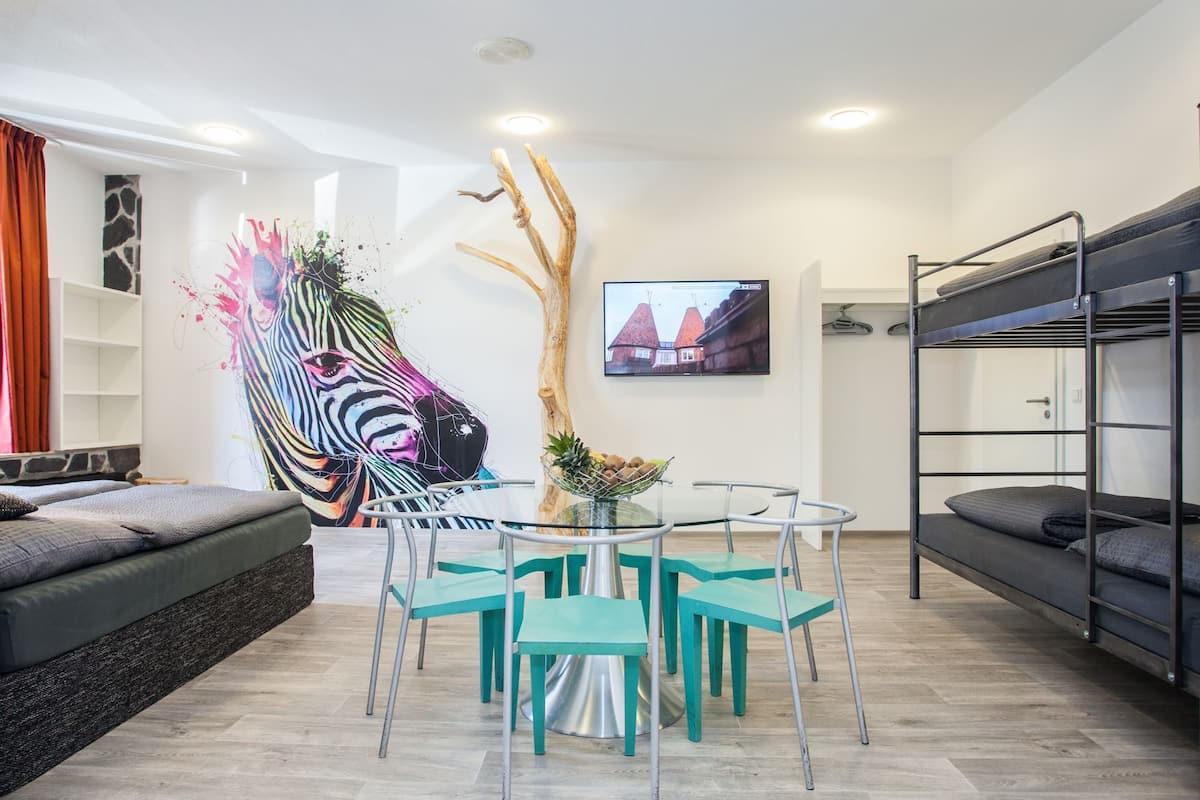 A modern living room with a zebra mural, a round table with chairs, a bunk bed, and a television displaying a house.