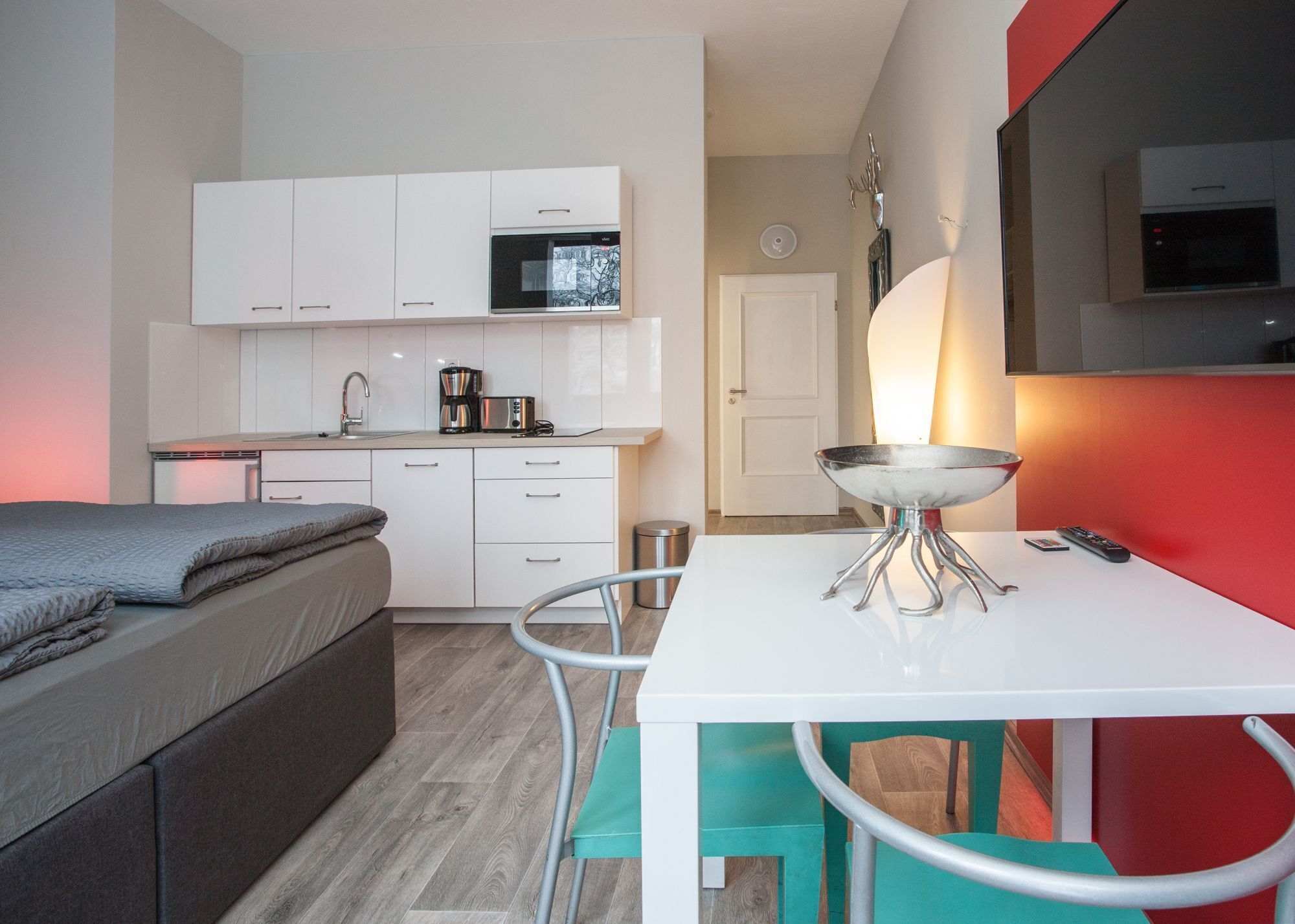 A compact kitchen with white cabinets, a microwave, a coffee maker, and a small dining table with a bowl.