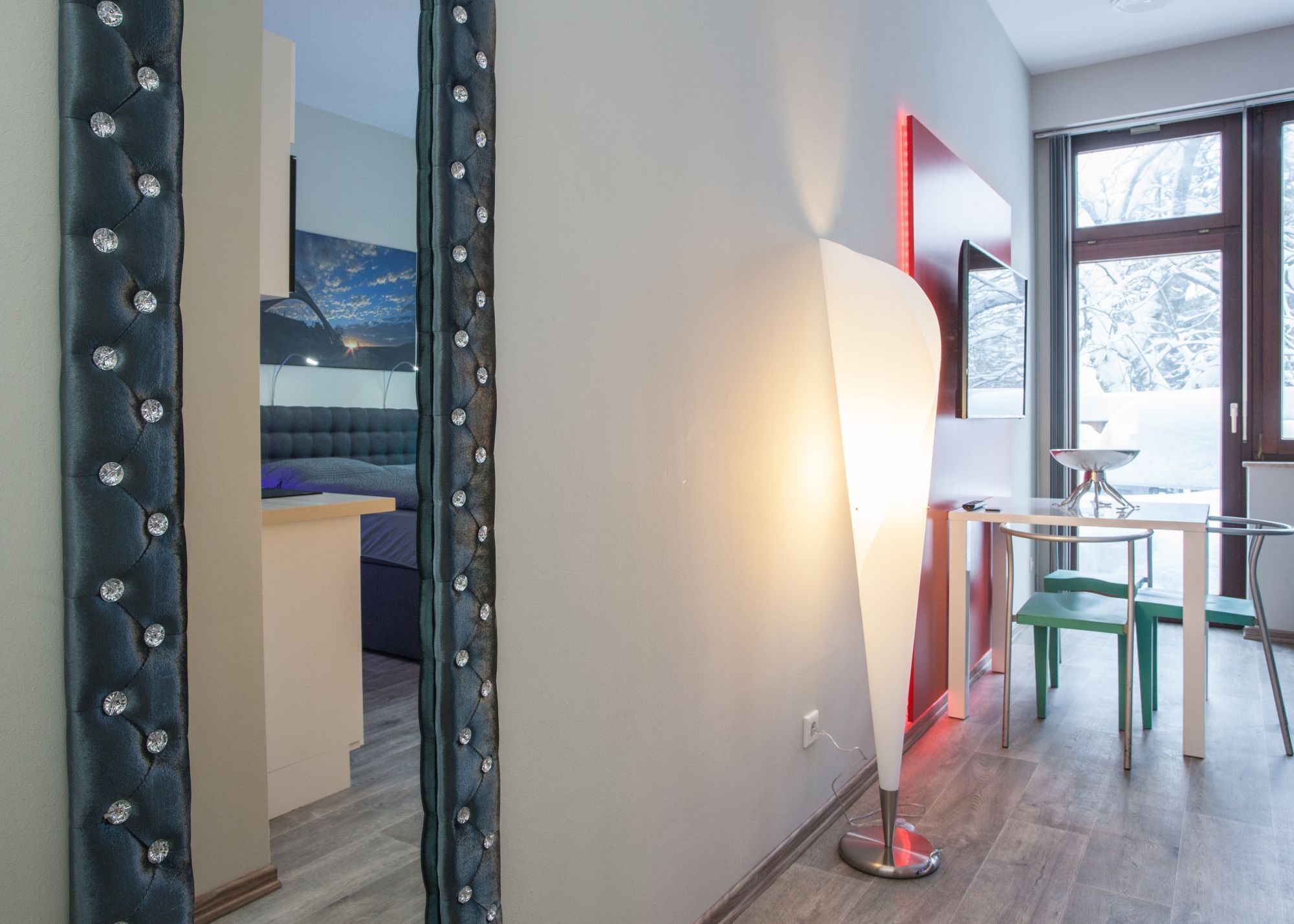 Ein modernes Hotelzimmer mit Bett, Schreibtisch und Stuhl. Ein großes Fenster bietet Blick auf Bäume.