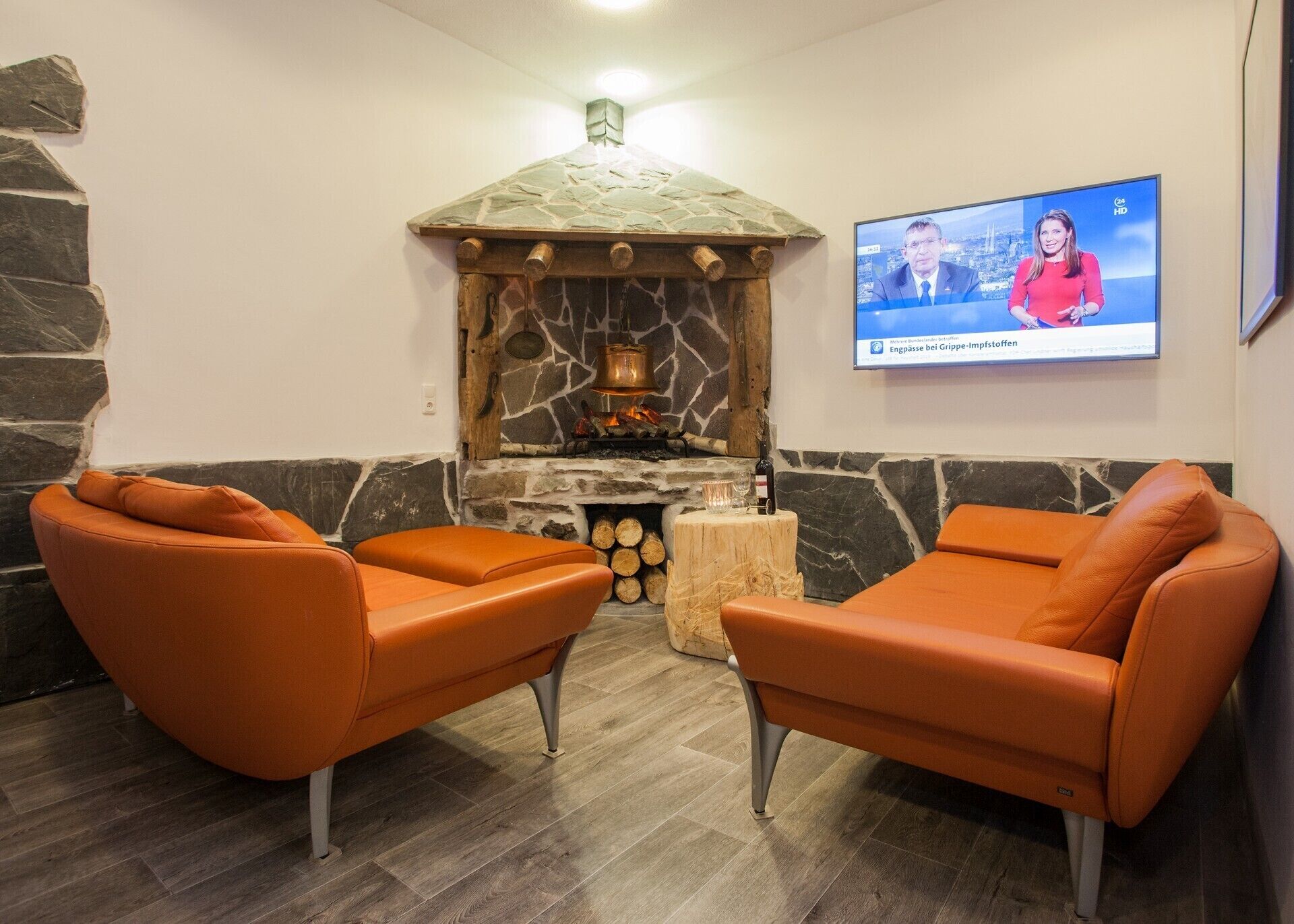 A room with a stone fireplace, two leather sofas, and a television mounted on the wall.
