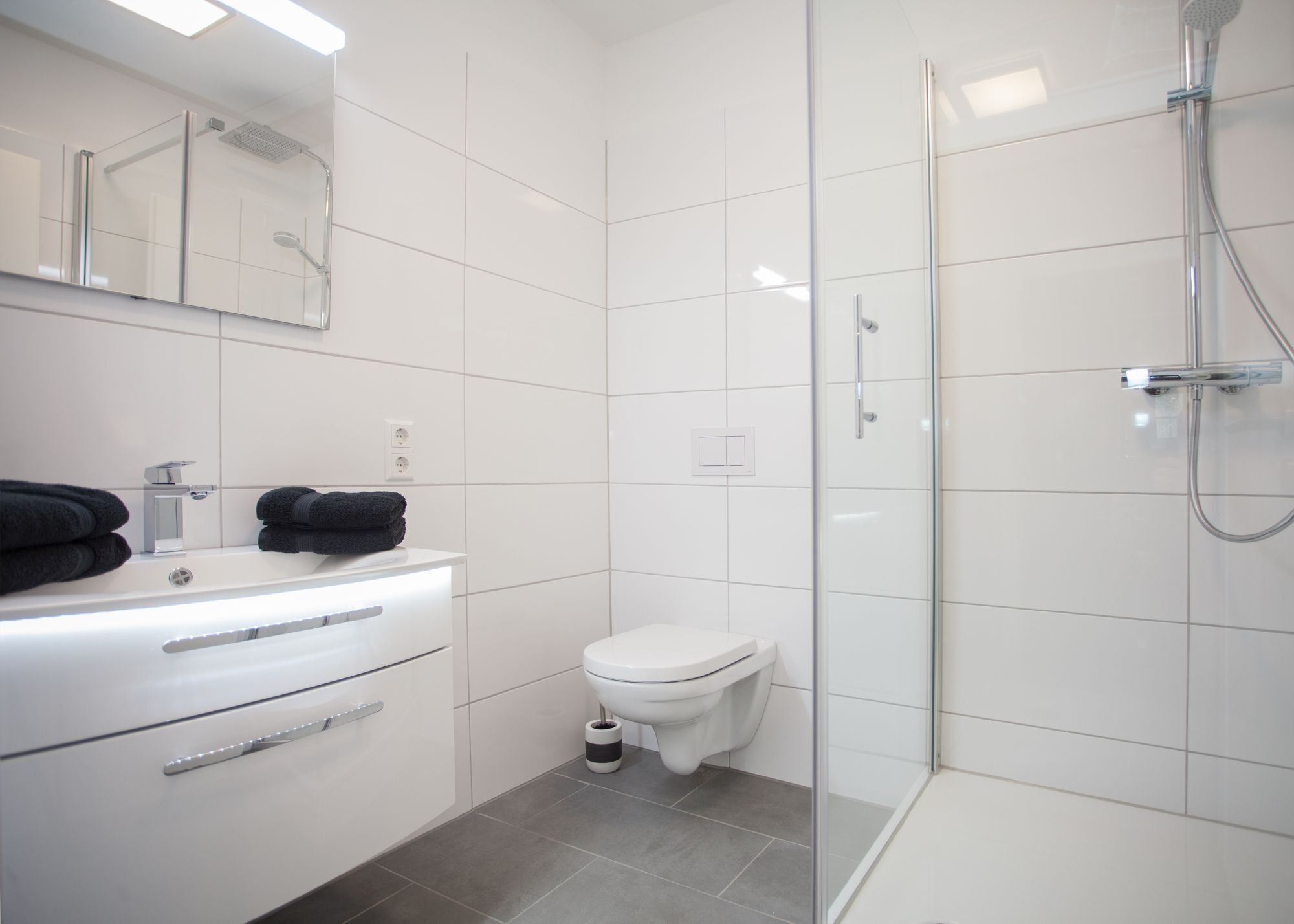 A modern bathroom with a glass-enclosed shower, a white sink with a mirror above it, and a toilet.