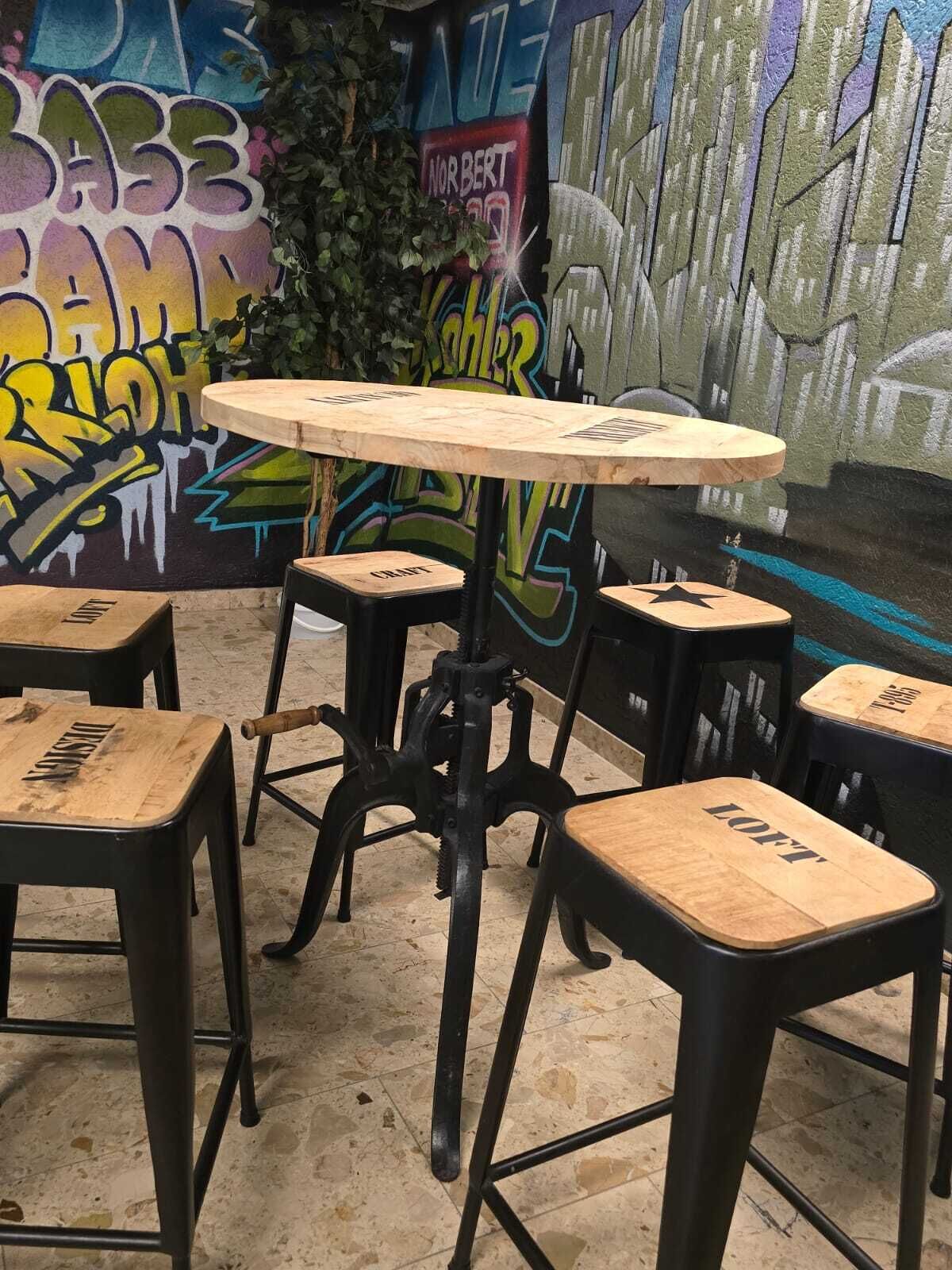 A small, rustic cafe with a graffiti-covered wall, a round wooden table, and four stools with 'LOFT' branding.