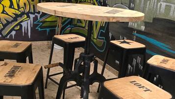 A small, rustic cafe with a graffiti-covered wall, a round wooden table, and four stools with 'LOFT' branding.