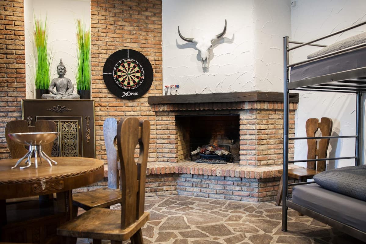 A room with a brick fireplace, a dartboard, a Buddha statue, and a bed with a metal frame.