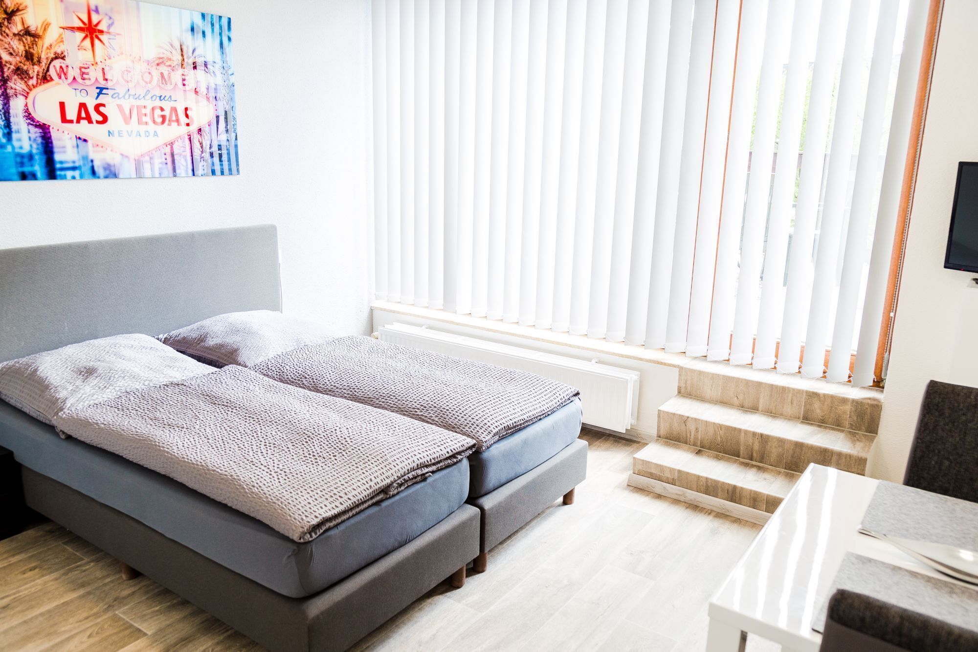 A modern bedroom with a bed, a window with blinds, a radiator, and a small table.