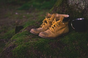 Braune Wanderschuhe mit gelben Schnürsenkeln auf einem moosbewachsenen Stein.