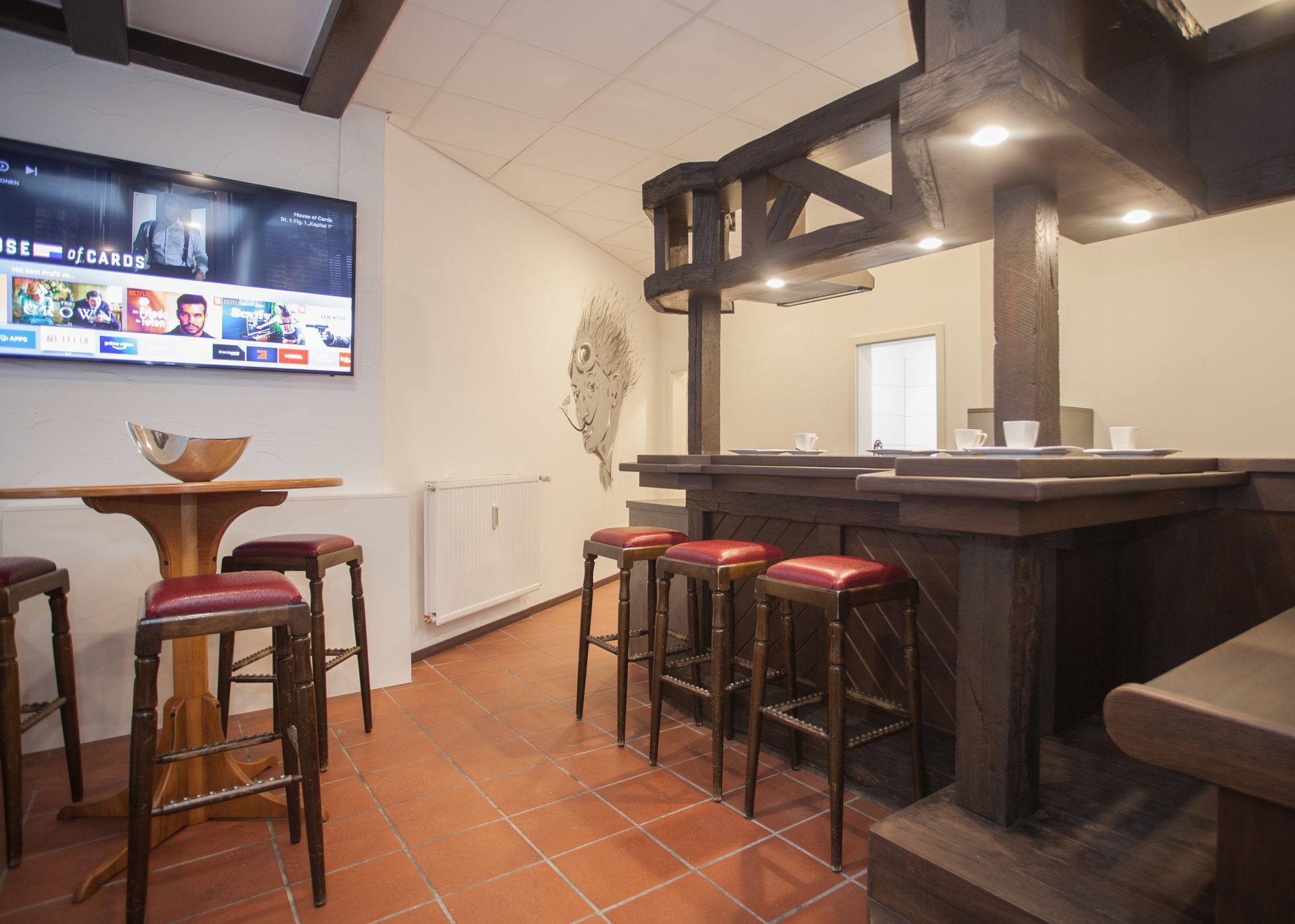 A bar area with wooden stools, a TV mounted on the wall, and a decorative wall piece.