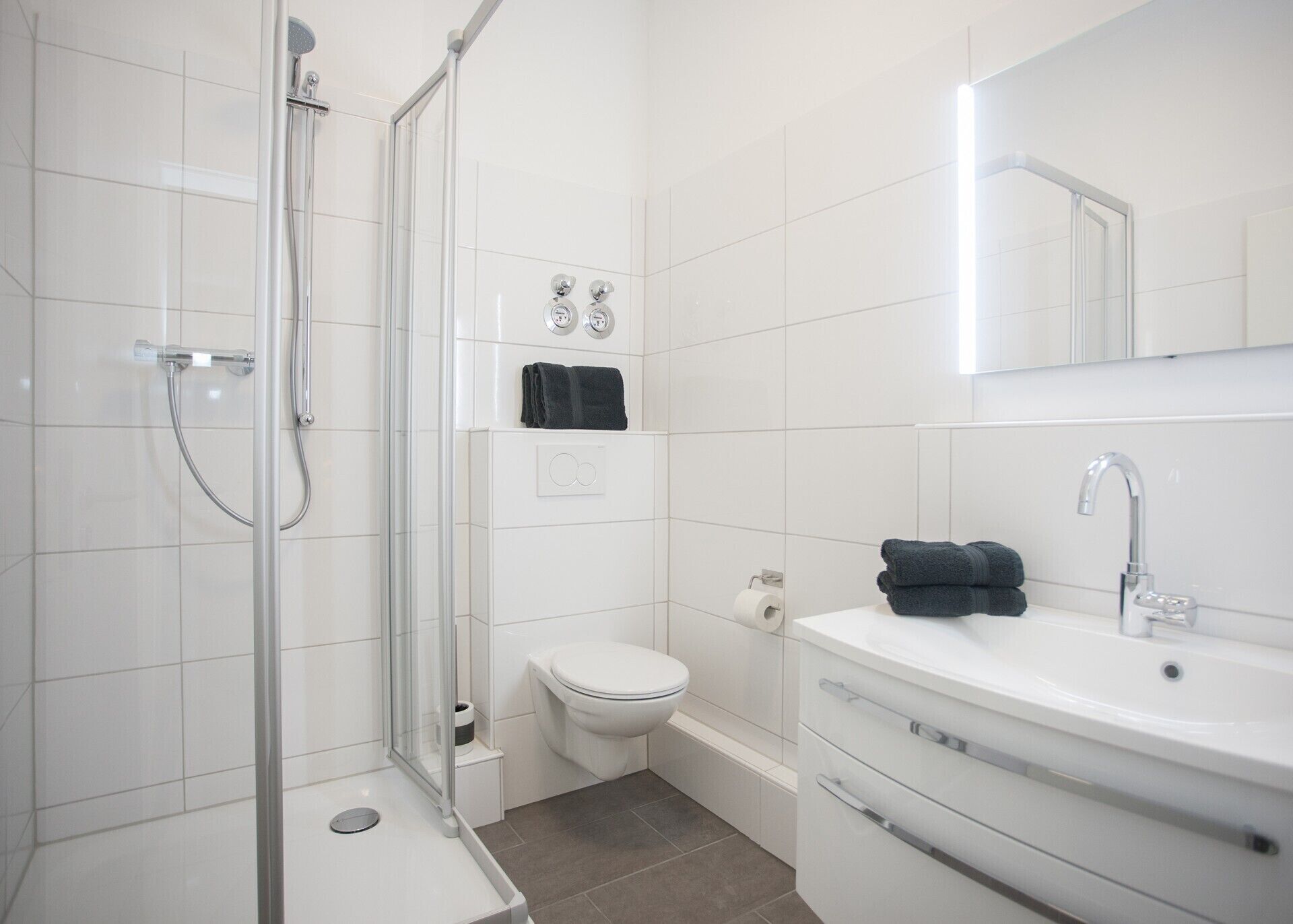 Un baño moderno con cabina de ducha de vidrio, inodoro y lavamanos con espejo superior.