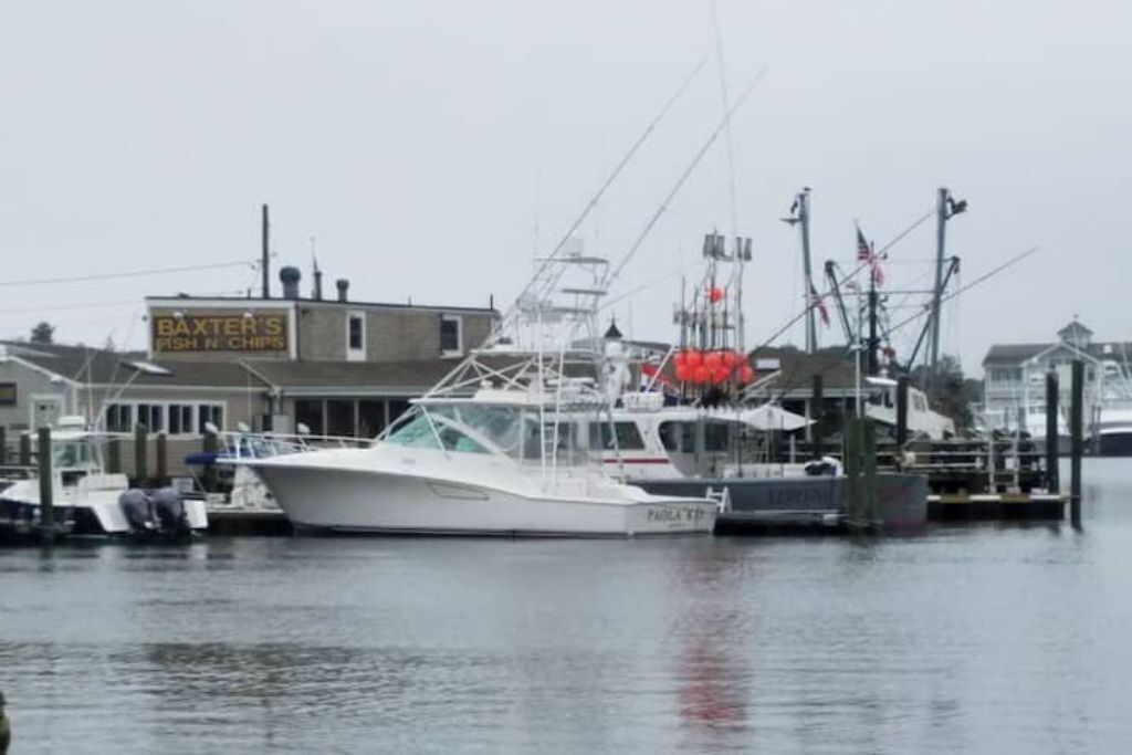 A marina with boats docked, a building labeled "BAXTER'S FISH N CHIPS," and a flagpole with flags.