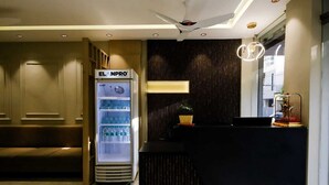 Zona de recepción de hotel con minibar, un sofá y una planta decorativa.