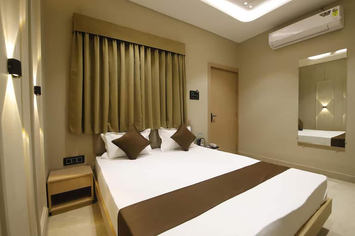 Una habitación de hotel con una cama grande, una mesita de noche, un espejo y un equipo de aire acondicionado.