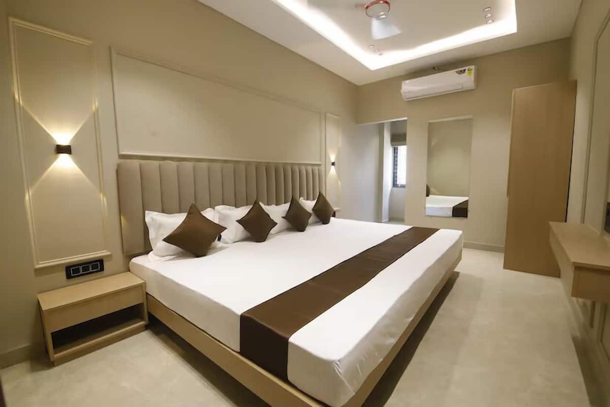 Habitación de hotel moderna con una cama grande, mesitas de noche, un mueble empotrado y un espejo, además de un equipo de aire acondicionado en la pared.