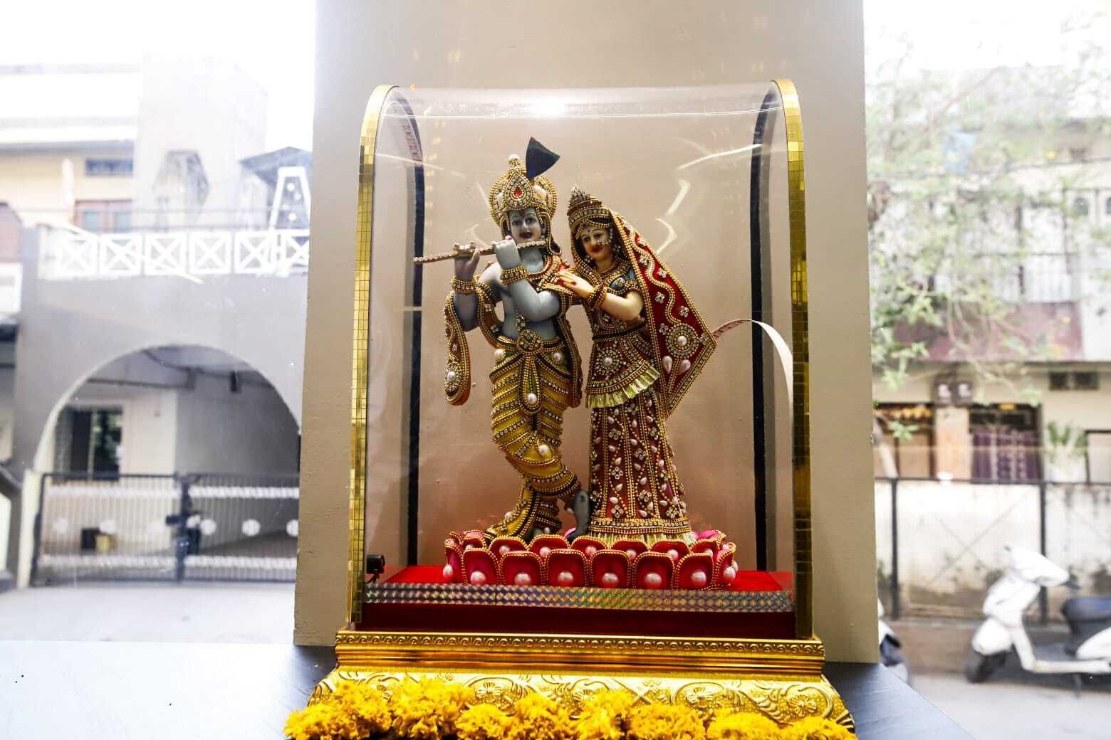 Una estatua de una deidad con un instrumento musical, sobre un pedestal rojo y dorado con un arreglo floral.