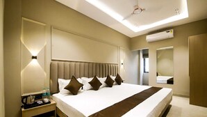 Una habitación de hotel con una cama grande, una mesita de noche con hervidor y un espejo.