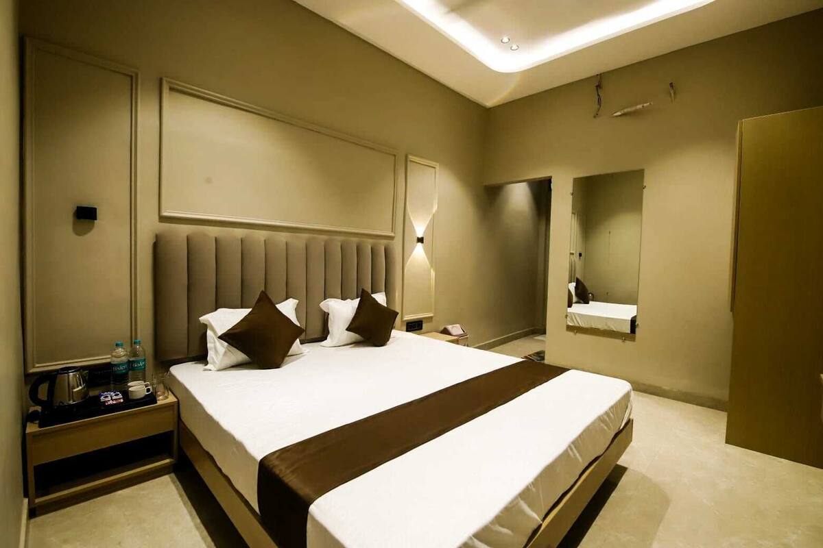 Una habitación de hotel con una cama grande, mesitas de noche, un espejo y un baño con lavabo y espejo.