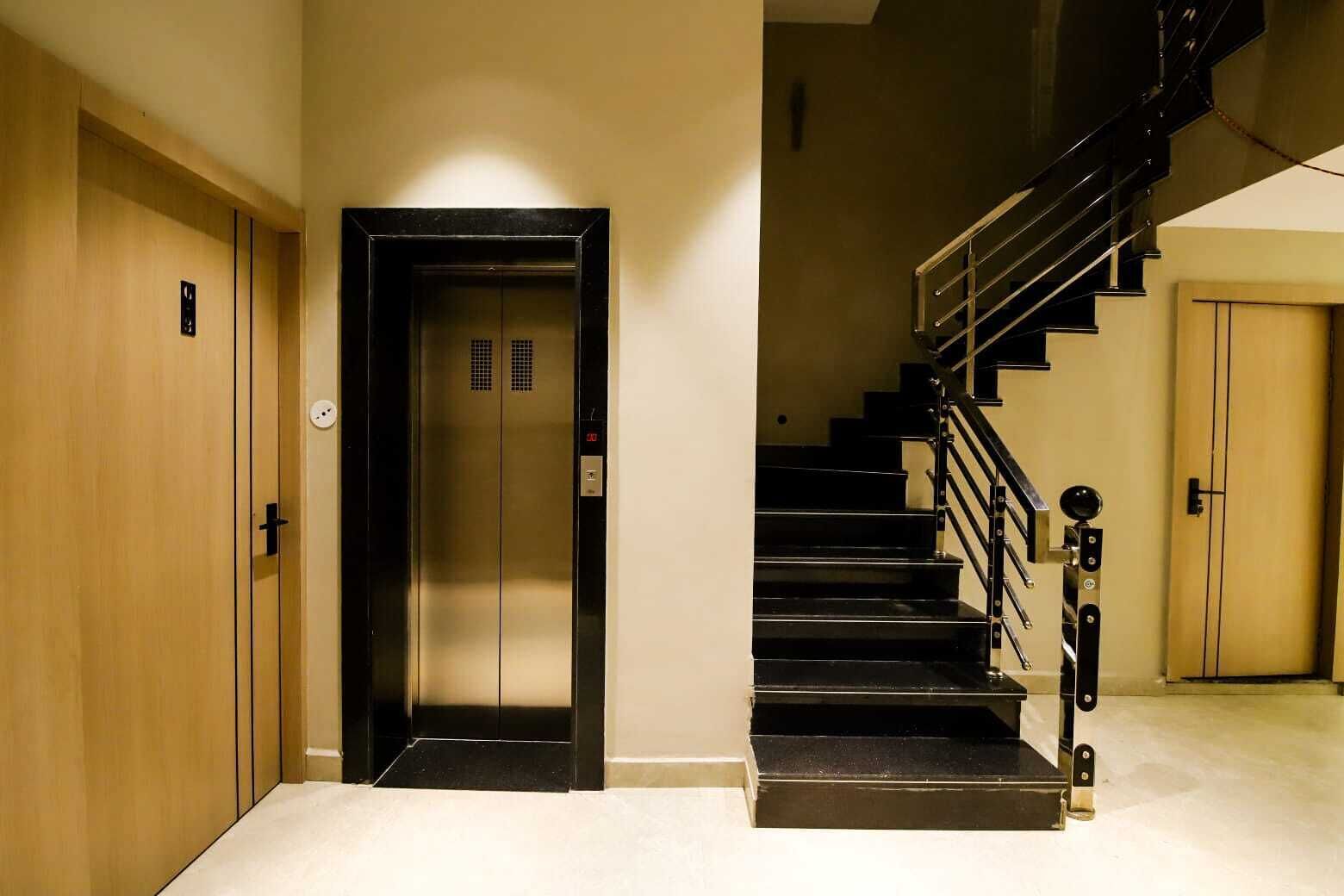 Un couloir d’hôtel avec une porte en bois, un ascenseur et un escalier muni d’une main courante.