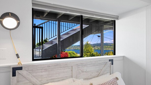 A bedroom with a large window overlooking a staircase and a scenic view of a lake and hills.