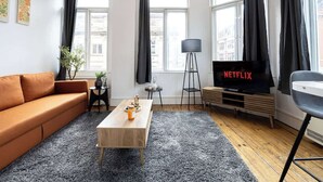 Una sala de estar con sofá, mesa de centro, televisor y ventanas amplias.