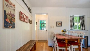 A dining area with a wooden bench, white chairs, and a table with a vase of flowers.