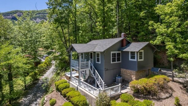 A two-story cabin with a balcony, surrounded by lush greenery and a river.