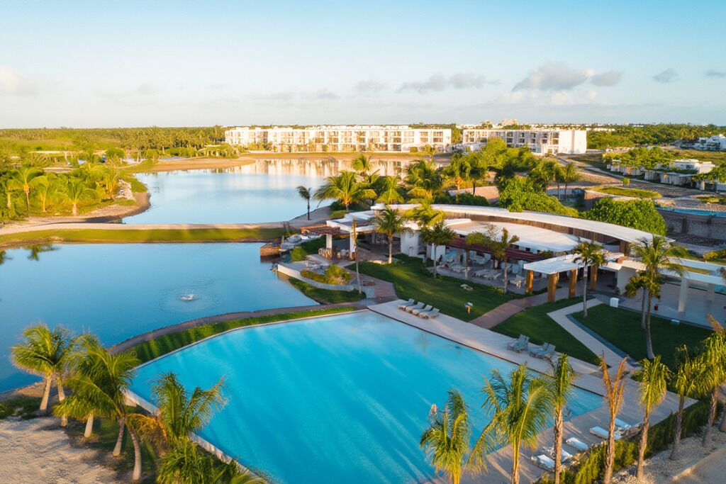 A resort with a large swimming pool, palm trees, and a building complex in the background.