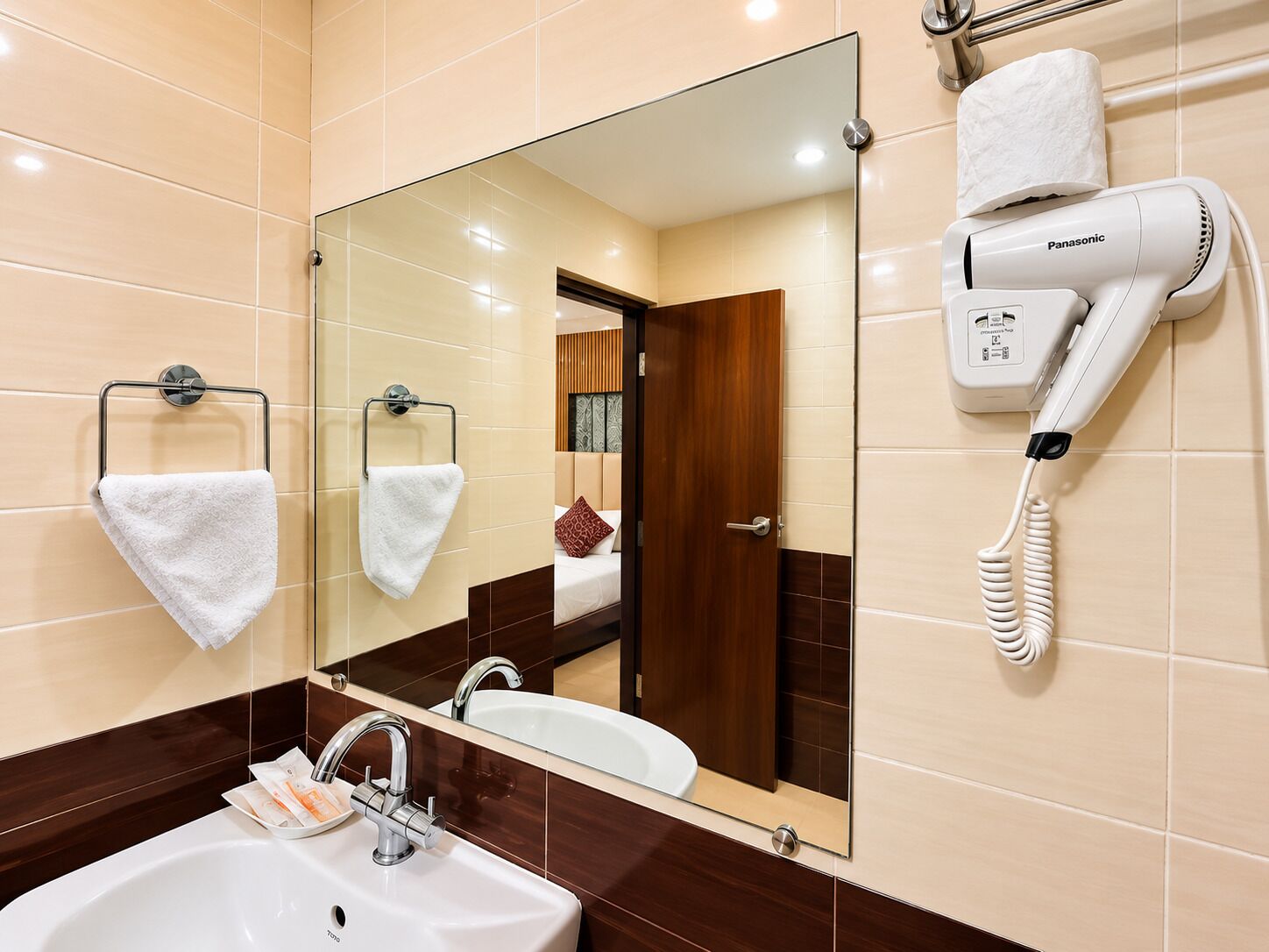 A hotel bathroom with a sink, mirror, towel rack, and a hairdryer.