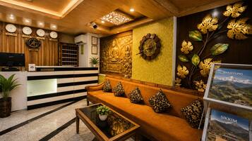 A reception area with a reception desk, a sofa with patterned cushions, a coffee table, and a wall with clocks and decorative elements.