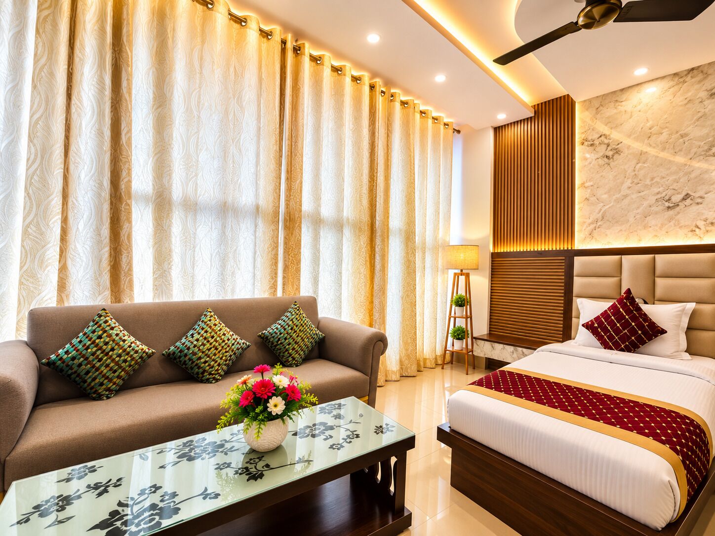 A hotel room with a sofa, a bed, a glass coffee table with a floral pattern, and a wall-mounted lamp.