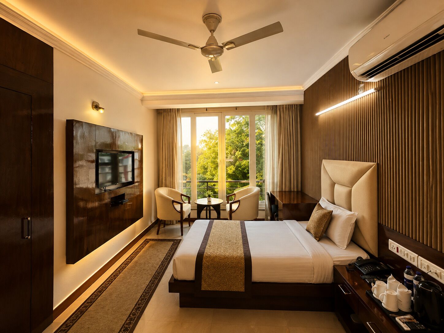 A hotel room with a bed, a TV, a ceiling fan, a balcony with a table and chairs, and a coffee station.