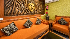 Una habitación con una estatua de Buda, un equipo de aire acondicionado, un extintor y dos sofás con cojines estampados.