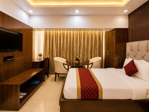 A hotel room with a bed, a TV, a desk with chairs, and a window with curtains.