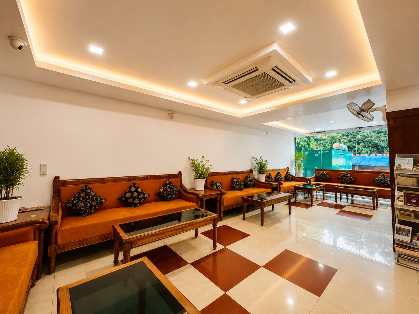 A hotel lobby with a checkered floor, wooden furniture, and a large window with a view of greenery.
