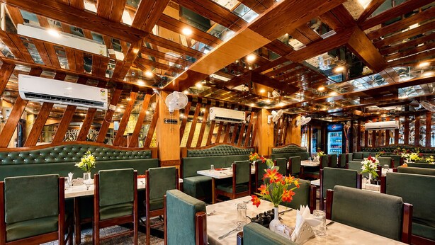 Un interior de restaurante con vigas de madera, asientos tapizados en verde y mesas dispuestas para comer.