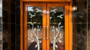 Puerta doble de madera con paneles de vidrio y motivos decorativos de hojas.