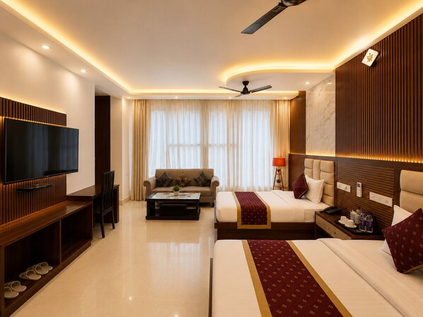 A hotel room with a flat-screen TV, a sofa, a bed with a red and gold bedspread, a ceiling fan, and a marble wall.