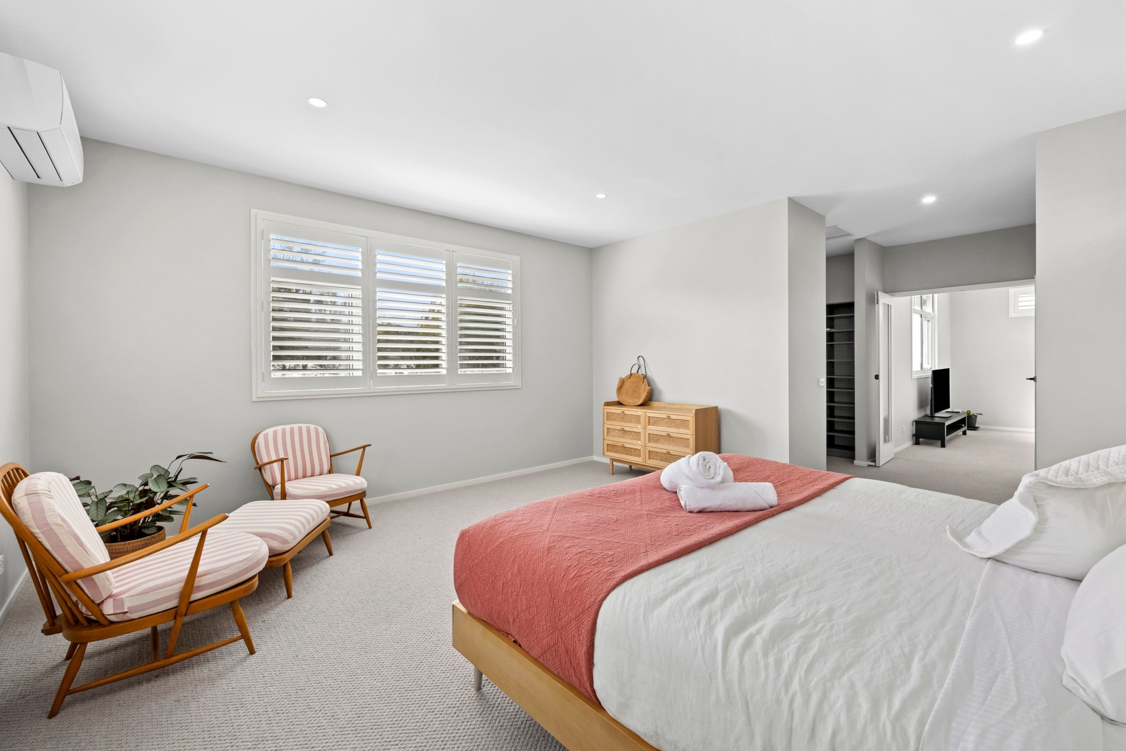 A bedroom with a bed, a seating area with chairs, a dresser, and a window with blinds.