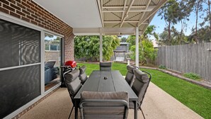 Ein überdachter Patio-Bereich mit Tisch, Stühlen, Grill und einer Schaukel.
