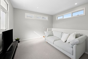 A modern living room with a grey sofa, a flat-screen TV, and a small plant. - Saltwater (Anglesea)