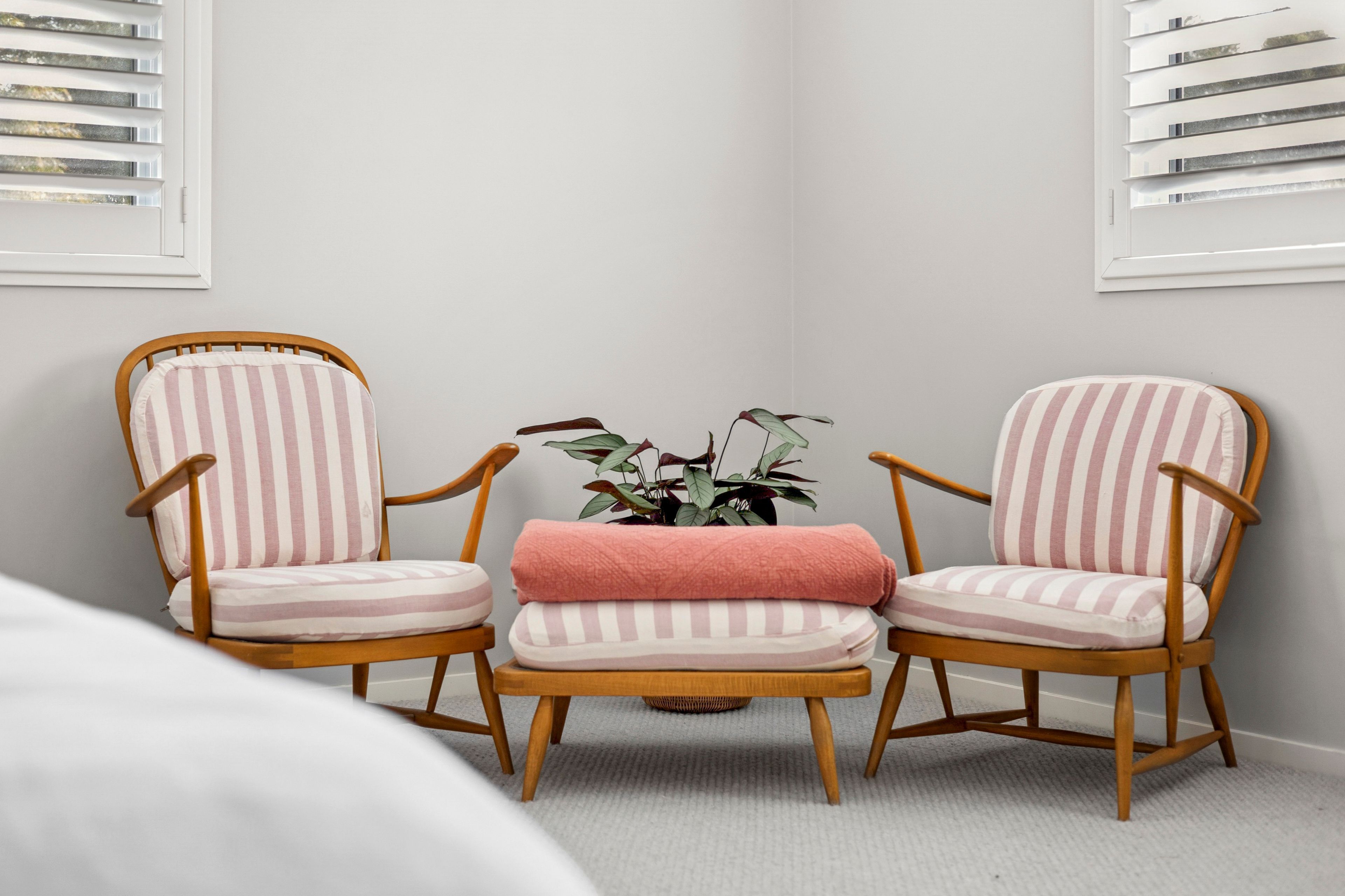 Une pièce avec deux fauteuils à rayures, une petite table sur laquelle repose un coussin rose, et une plante en pot.