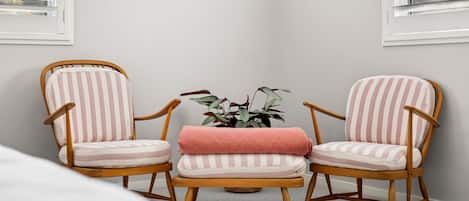 Ein Zimmer mit zwei gestreiften Sesseln, einem kleinen Tisch mit rosa Kissen und einer Topfpflanze.