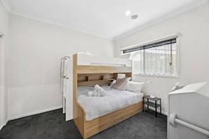 A bunk bed with a wooden frame and white bedding, a small bedside table with a lamp, a window with lace curtains, and a white wardrobe. - Saltwater (Anglesea)