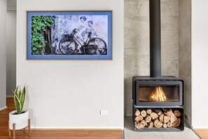 A room with a framed picture of a bicycle, a potted plant, and a wood-burning stove.