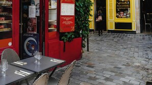 Un café en plein air avec des tables et des chaises, un auvent rouge et une façade jaune ornée d’une enseigne.