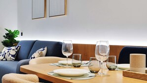 Un coin repas avec une table en bois dressée pour deux personnes, deux tableaux encadrés au mur et un canapé bleu agrémenté de coussins à motifs.