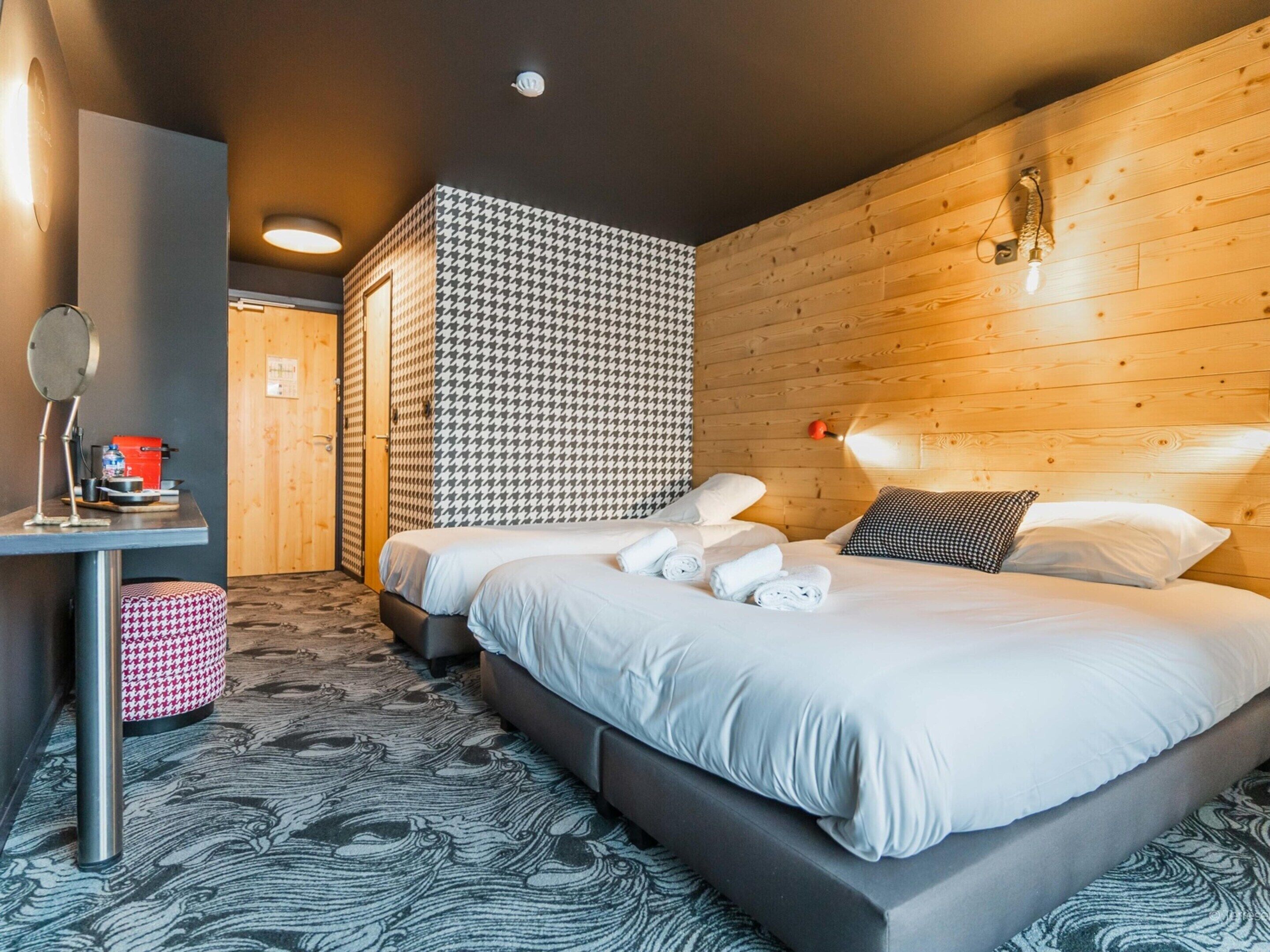 Quarto de hotel moderno com uma cama grande, cabeceira de madeira e papel de parede estampado.