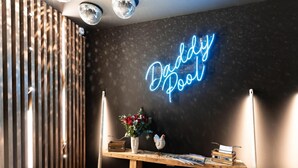 A room with a neon sign reading "Buddy Pool," a wooden table with books and a vase of flowers, and a wooden slat wall. - Delightful Apartment in Saint Chaffrey (Saint-Chaffrey)